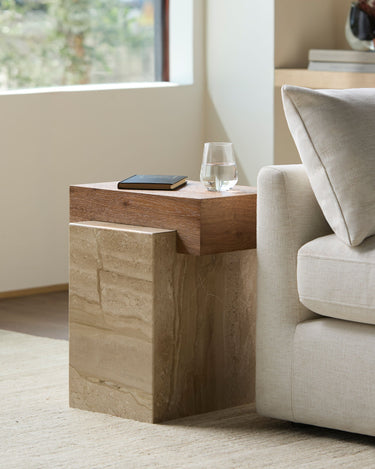Wooden side table with a glass and phone next to a beige sofa in a living room.