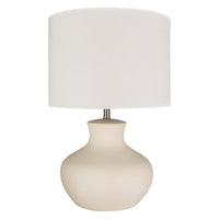A beige Baldwin table lamp with a cylindrical linen shade and a cream glazed ceramic body, isolated on a white background.