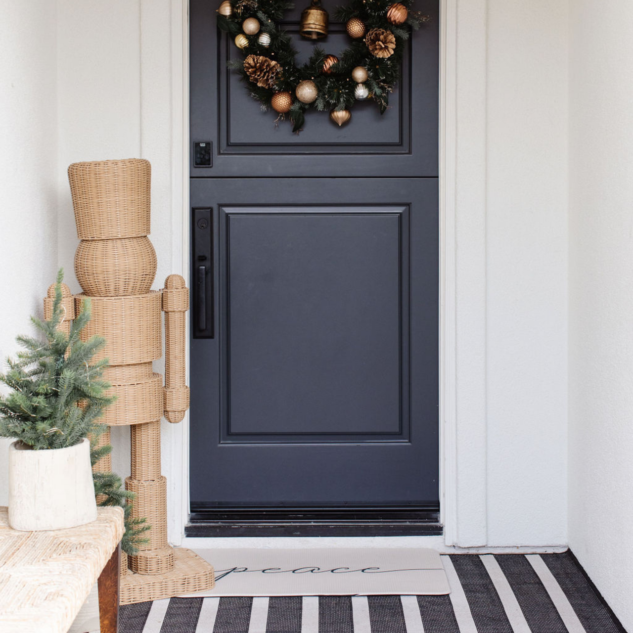 Decorative wreath on a black door with a Christmas tree and decorative items on a white wall.