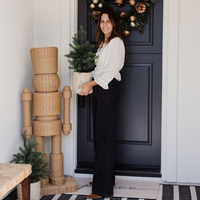Woman standing in front of a decorated door with Christmas wreath and plants.