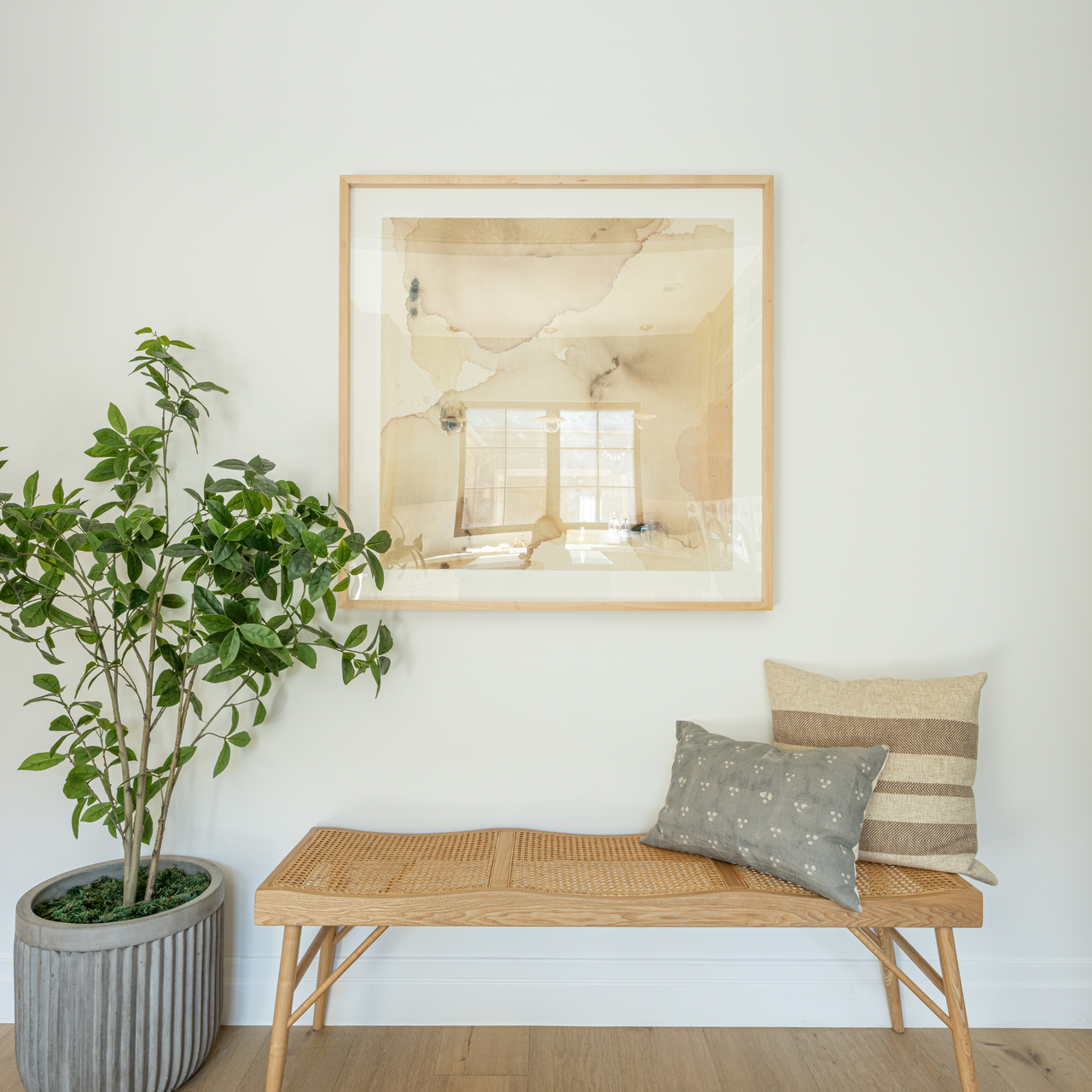 Wooden bench with pillows against a white wall with a framed picture
