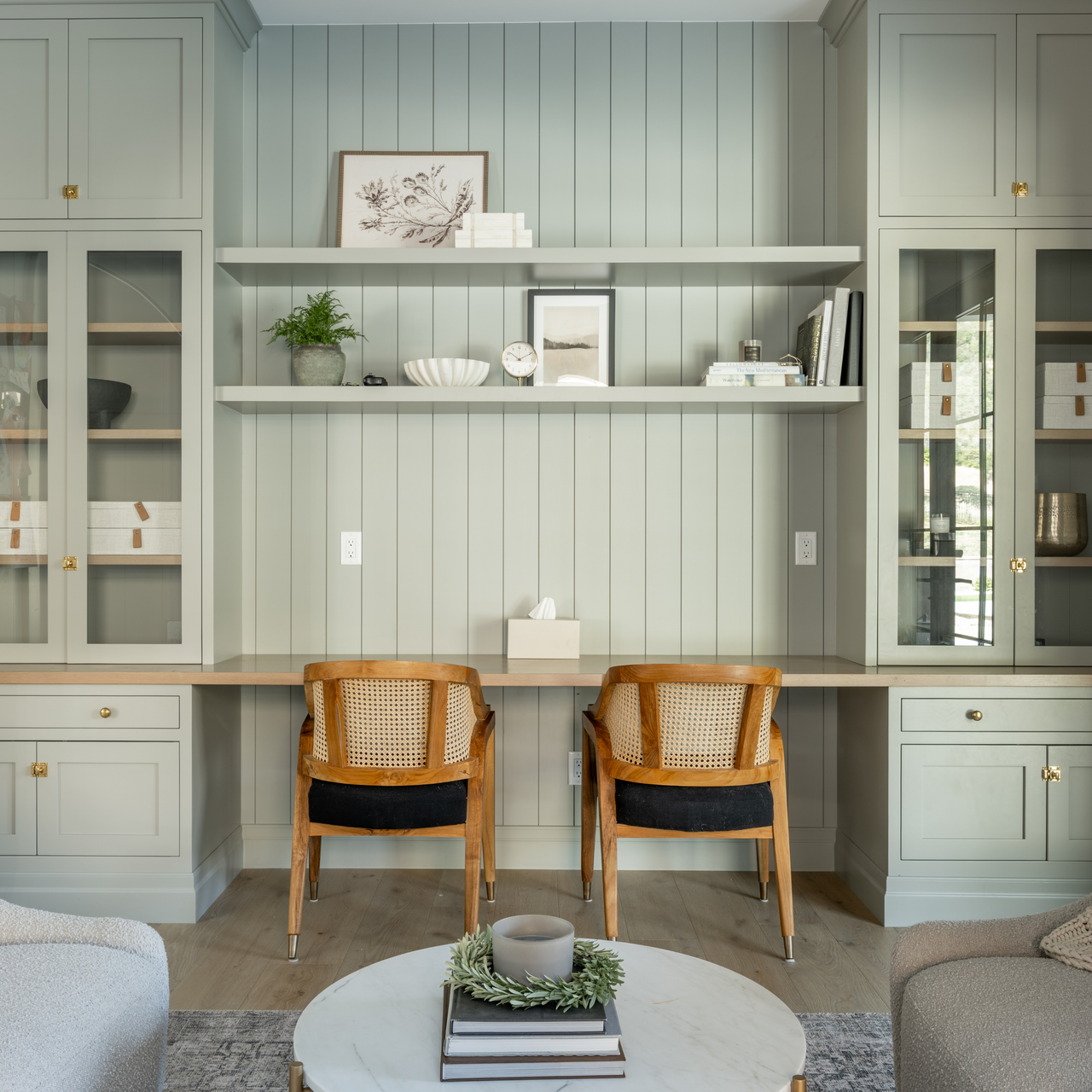 Modern home office with light green walls, wooden chairs, and glass cabinets.