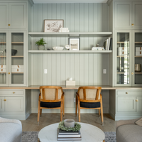 Modern home office with light green walls, wooden chairs, and glass cabinets.