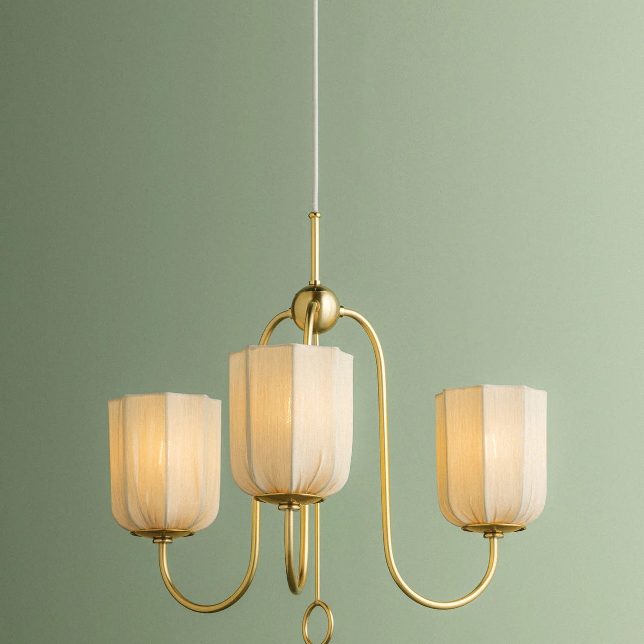 Gold chandelier with three light fixtures against a green wall