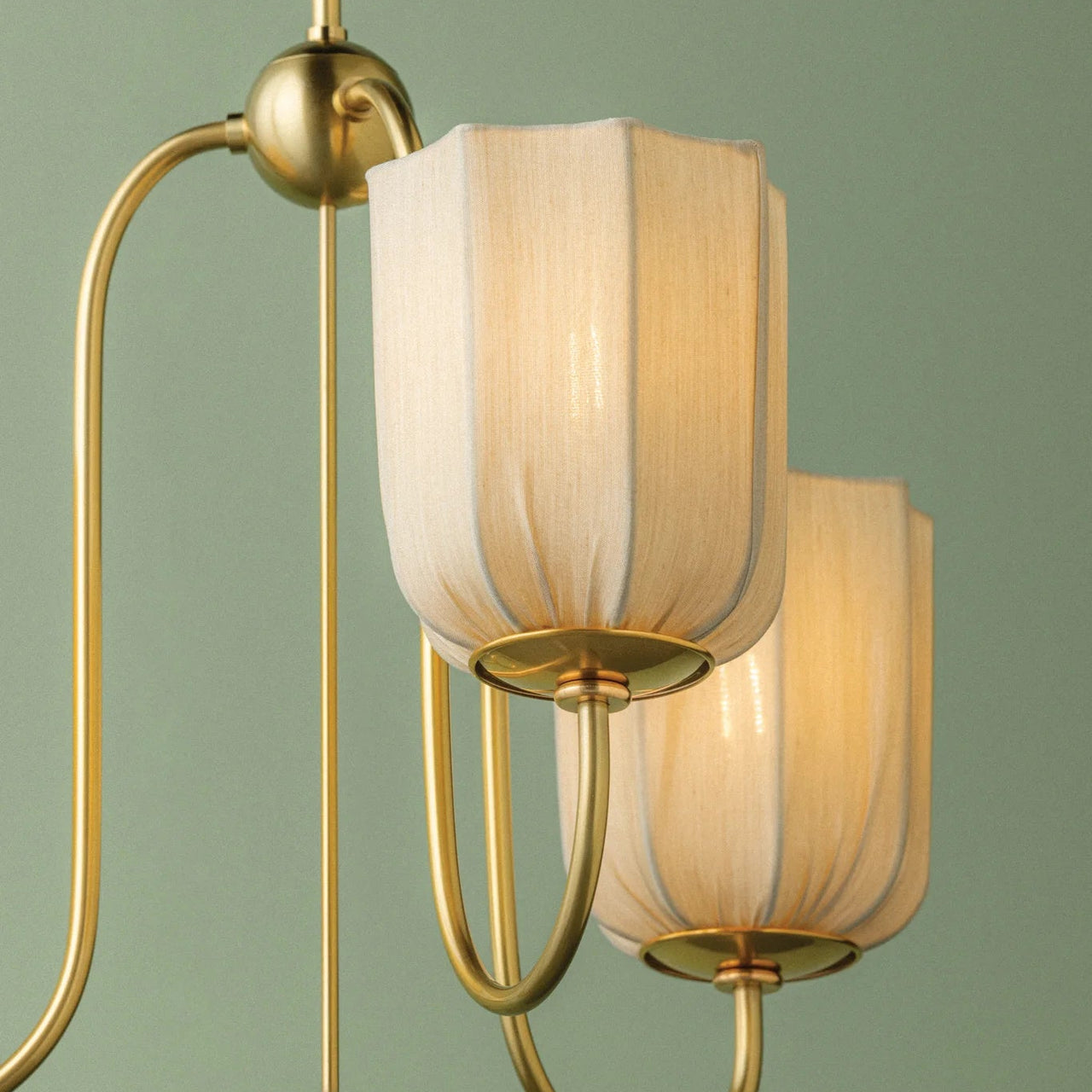 Modern chandelier with gold fixture and beige lampshades on a green background