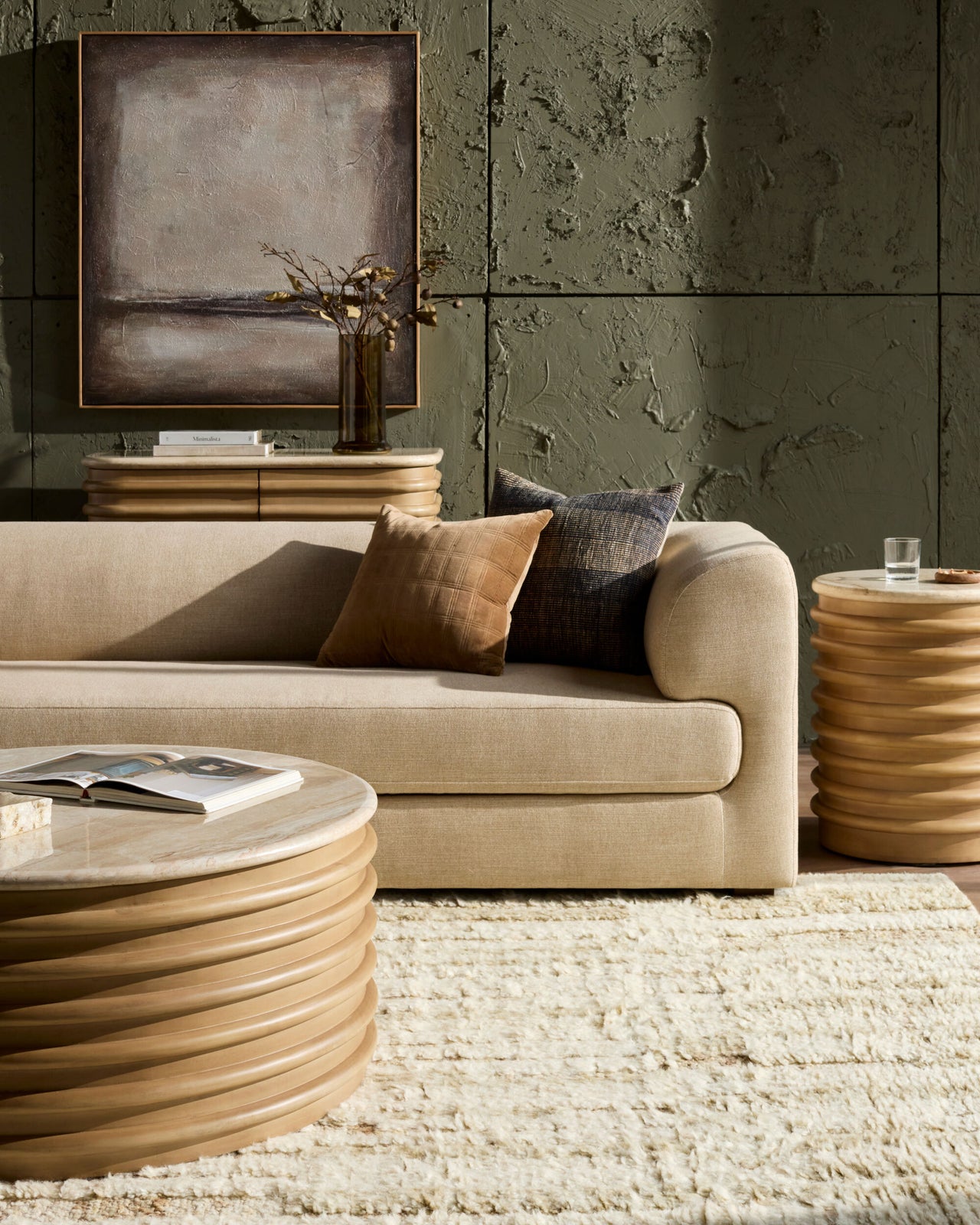 Modern living room with a beige sofa, round coffee table, and abstract painting on a textured wall.