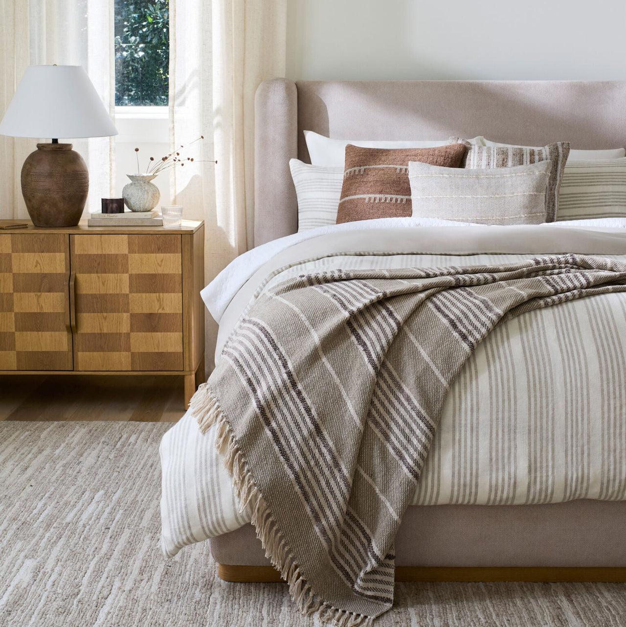 Neatly made bed with striped bedding and a blanket in a bedroom setting.
